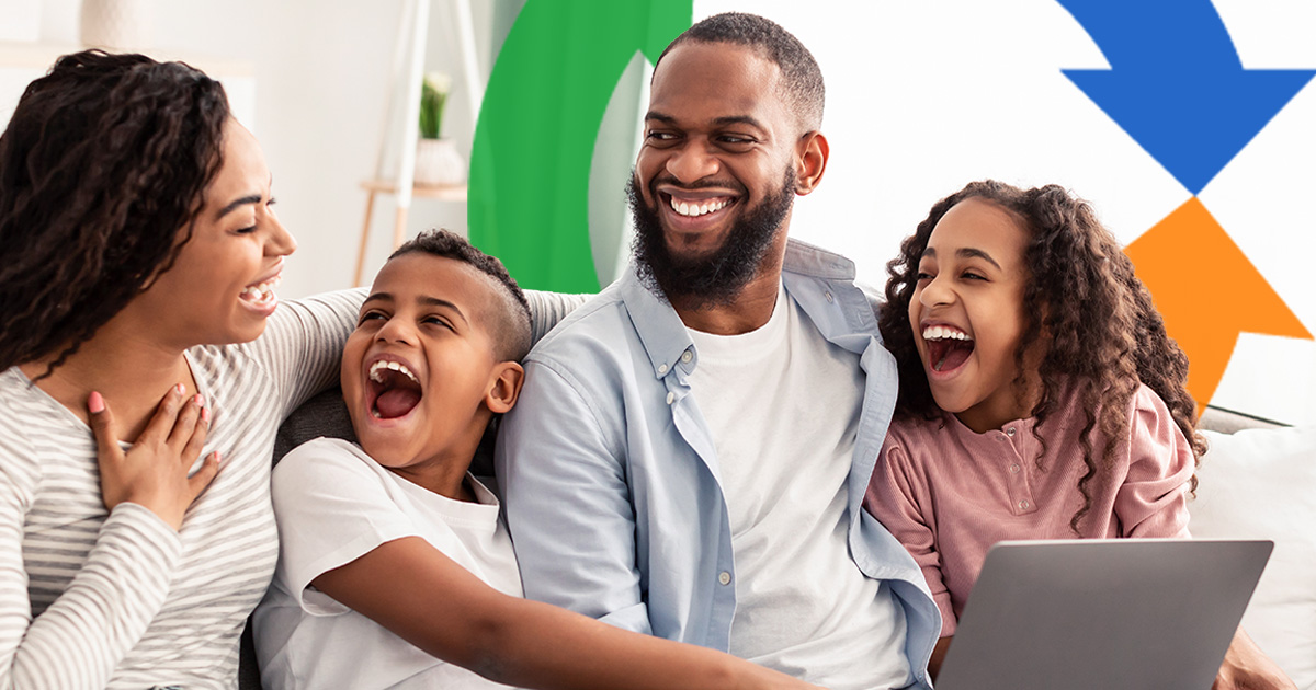 A family sits on a couch sharing a laugh while using a laptop.