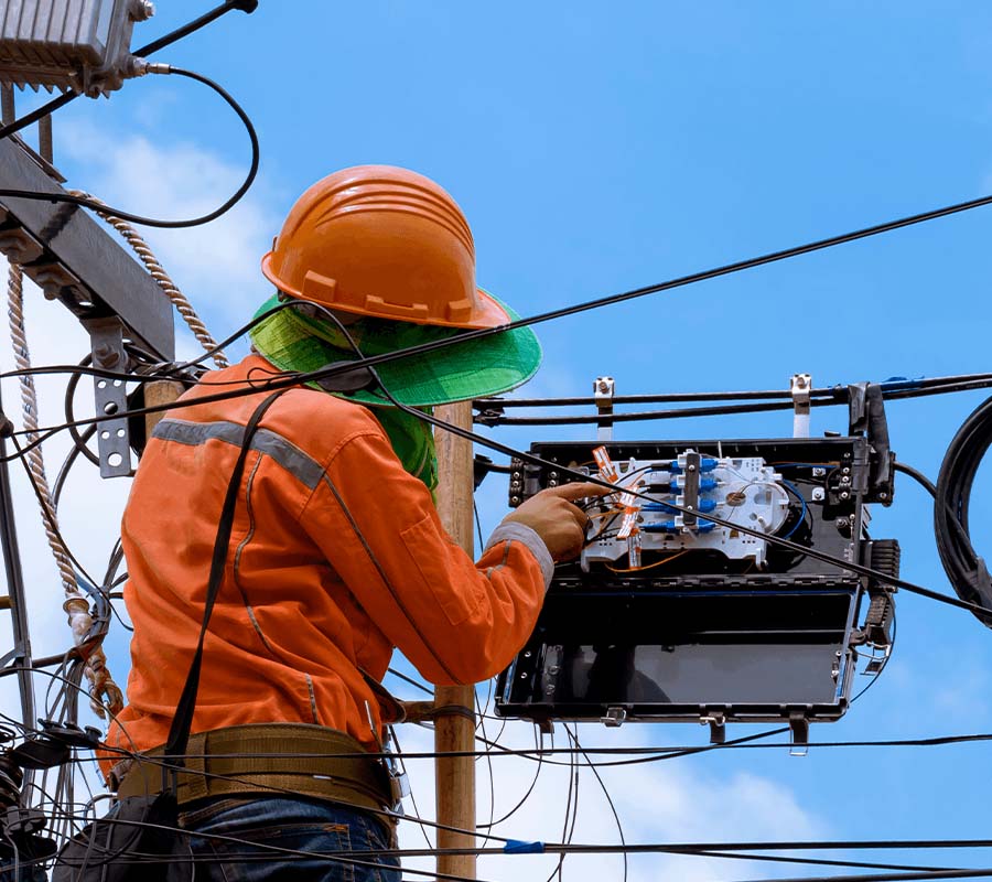 A man wearing a high-vis shirt and hardhat works on electrical wires.