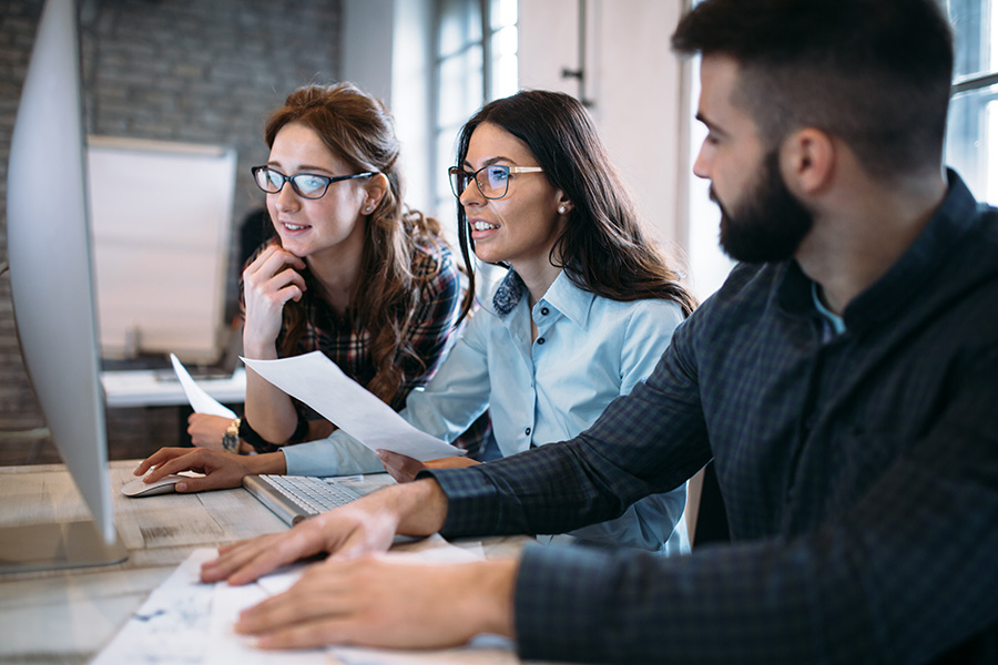 A team of employees work together on their computers while smiling.